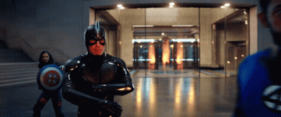 A Man In A Superhero Costume Is Holding A Shield In Front Of A Glass Door . GIF