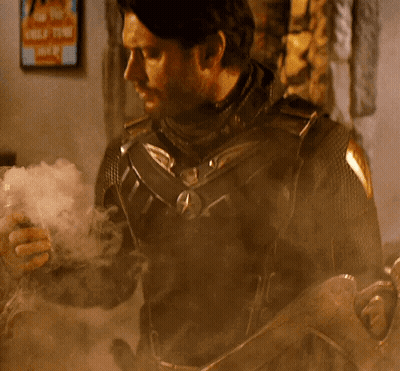 A Man In A Superhero Costume Is Smoking A Cigarette While Holding A Gun . GIF