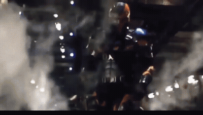 A Man In A Superhero Costume Is Standing In A Dark Room With Smoke Coming Out Of It GIF