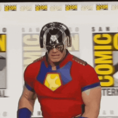 A Man In A Superhero Costume Is Standing In Front Of A Comic Con Poster . GIF