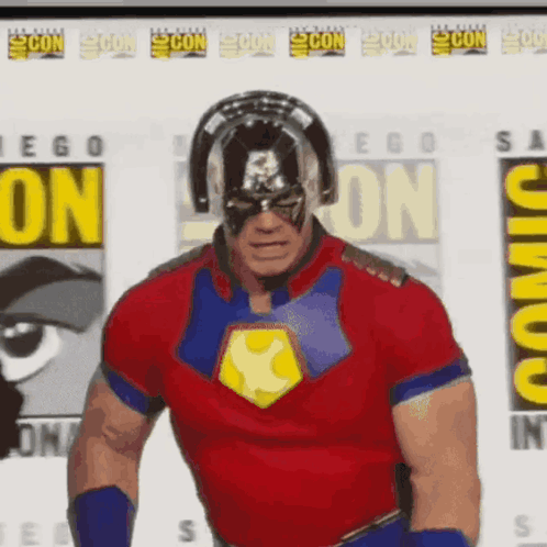 A Man In A Superhero Costume Is Standing In Front Of A Comic Con Sign GIF