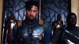 A Man In A Superhero Costume Is Standing In Front Of A Group Of Men . GIF