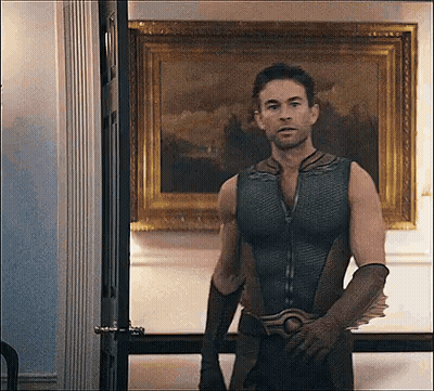A Man In A Superhero Costume Is Standing In Front Of A Painting In A Room . GIF