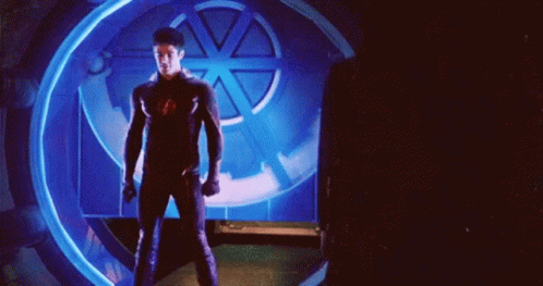 A Man In A Superhero Suit Is Standing In Front Of A Blue Light GIF