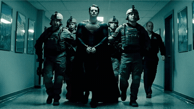 A Man In A Superman Costume Is Being Escorted Down A Hallway By Police Officers GIF