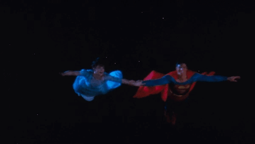 A Man In A Superman Costume Is Holding A Woman 'S Hand GIF