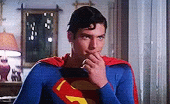 A Man In A Superman Costume Is Holding His Hand To His Mouth GIF