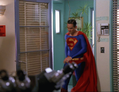 A Man In A Superman Costume Is Standing In Front Of A Door GIF