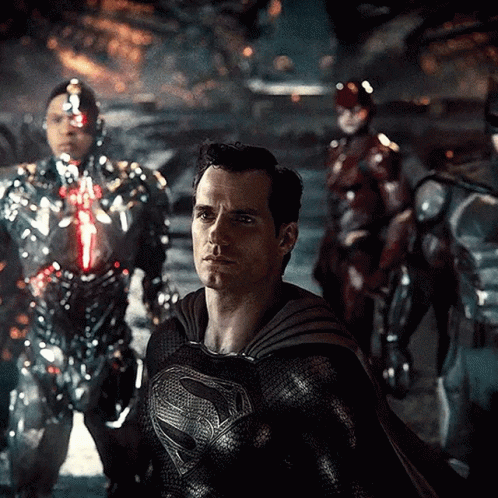 A Man In A Superman Costume Is Standing In Front Of A Group Of Robots GIF