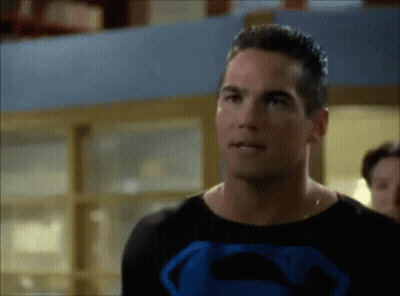 A Man In A Superman Costume Is Standing In Front Of A Window . GIF