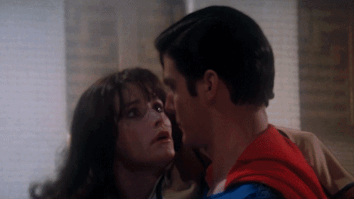 A Man In A Superman Costume Kisses A Woman GIF
