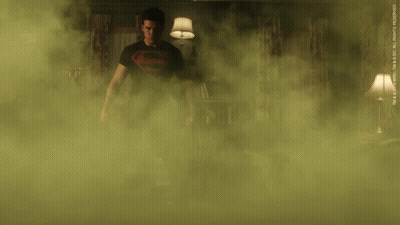 A Man In A Superman Shirt Is Standing In A Room Surrounded By Smoke GIF