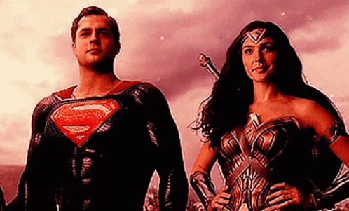 A Man In A Superman Suit And A Woman In A Wonder Woman Outfit Are Standing Next To Each Other . GIF