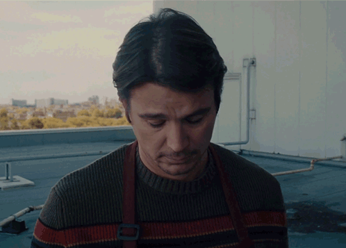 A Man In A Sweater And Apron Looks Down GIF