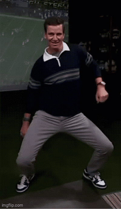 A Man In A Sweater And Gray Pants Is Dancing In Front Of A Screen . GIF