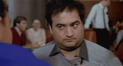 A Man In A Sweater And Tie Is Looking At Another Man . GIF