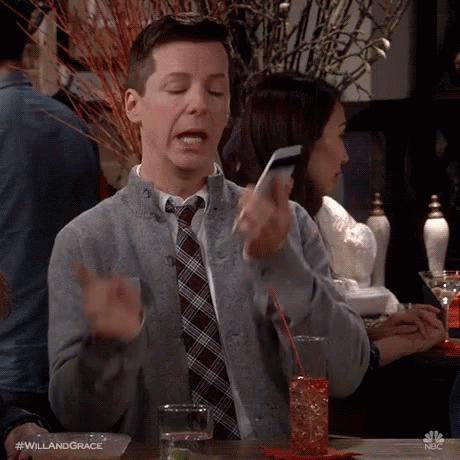 A Man In A Sweater And Tie Is Sitting At A Table Holding A Cell Phone . GIF