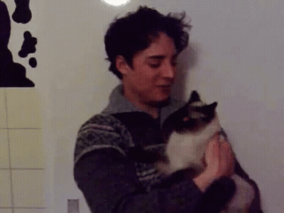 A Man In A Sweater Is Holding A Cat In His Hands GIF