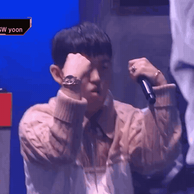 A Man In A Sweater Is Holding A Microphone And Covering His Face . GIF