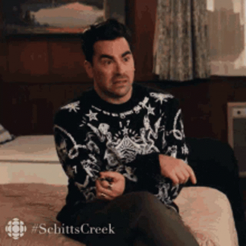 A Man In A Sweater Is Sitting On A Couch With His Legs Crossed . GIF