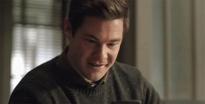 A Man In A Sweater Is Smiling And Looking At His Phone GIF