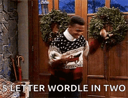 A Man In A Sweater Is Standing In Front Of A Door Holding A Wreath And Saying 5 Letter Wordle In Two . GIF