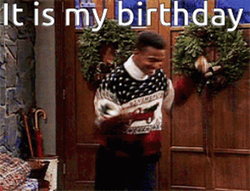 A Man In A Sweater Is Standing In Front Of A Door With A Wreath And The Words It Is My Birthday GIF