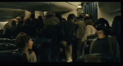 A Man In A Sweater Is Walking Through A Crowd Of People On An Airplane GIF