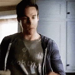 A Man In A T-Shirt And A Hoodie Is Standing In A Kitchen . GIF