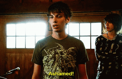 A Man In A T-Shirt That Says " Ashamed " Stands In Front Of A Microphone GIF