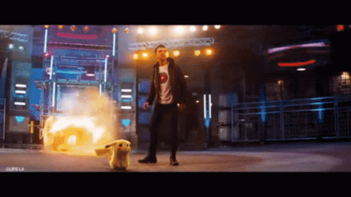 A Man In A T-Shirt With A Smiley Face On It Is Standing Next To A Pikachu GIF