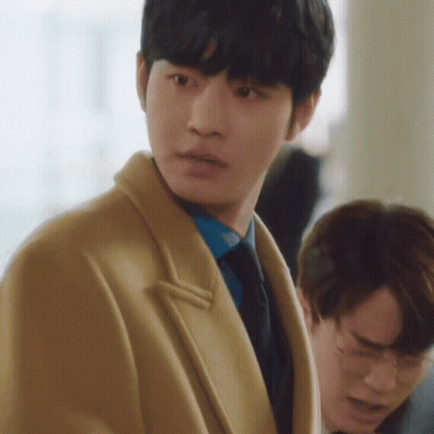 A Man In A Tan Coat And Blue Tie Is Standing Next To Another Man In A Suit . GIF
