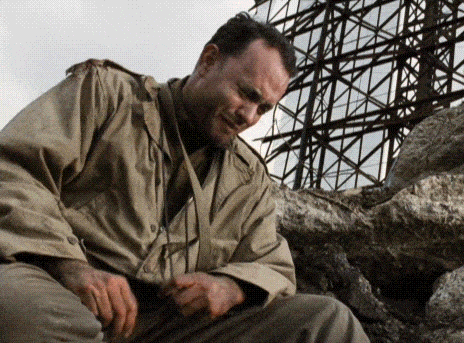 A Man In A Tan Jacket Is Sitting On A Pile Of Rocks Looking Down . GIF
