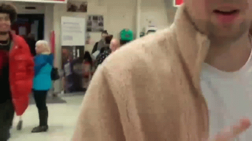 A Man In A Tan Jacket Is Standing In A Crowd GIF
