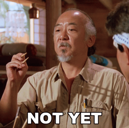 A Man In A Tan Shirt Holds Chopsticks In His Hand And Says " Not Yet " GIF