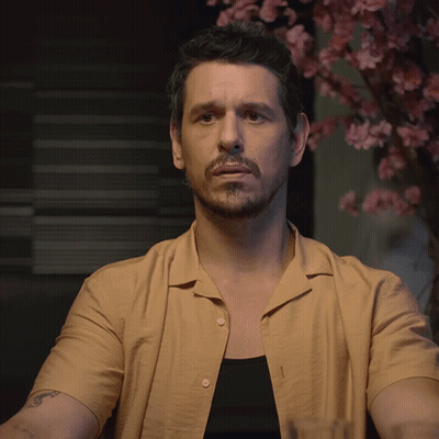 A Man In A Tan Shirt Holds Up His Hand GIF