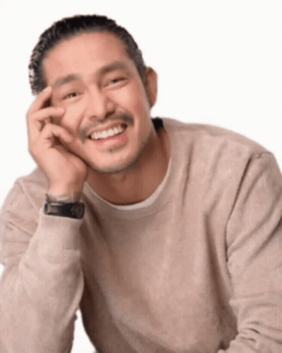 A Man In A Tan Sweater Is Smiling With His Hand On His Chin GIF