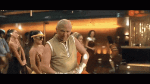 A Man In A Tan Tank Top Is Dancing In Front Of A Crowd GIF