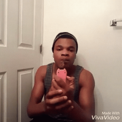 A Man In A Tank Top Is Holding A Pink Phone In Front Of A White Door Made With Vivavideo GIF
