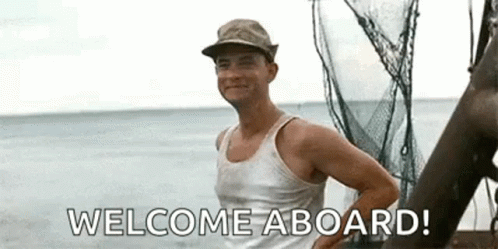 A Man In A Tank Top Is Standing On A Boat In The Ocean And Saying Welcome Aboard . GIF