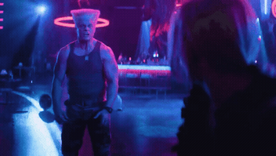 A Man In A Tank Top Stands In A Dark Room GIF