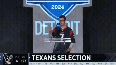 A Man In A Texans Jersey Stands At A Podium In Front Of A Screen That Says Texans Selection GIF
