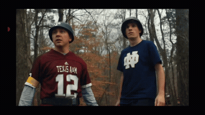 A Man In A Texas A & M Jersey Stands Next To Another Man GIF