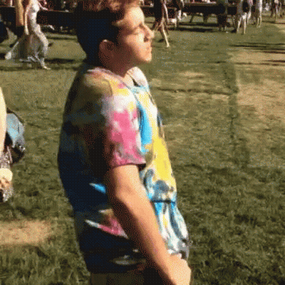 A Man In A Tie Dye Shirt Stands In The Grass GIF