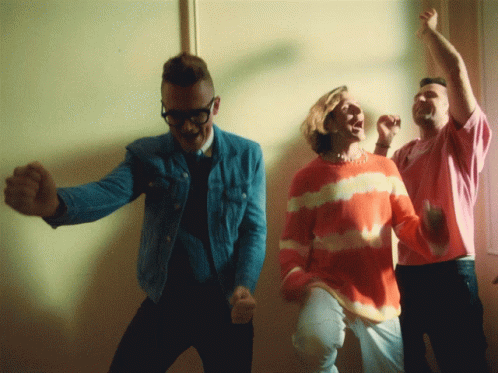 A Man In A Tie Dye Sweater Is Dancing With Two Other People GIF