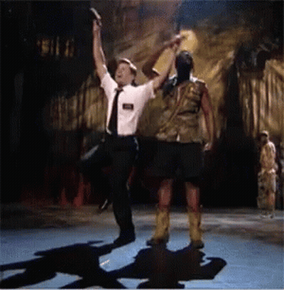 A Man In A Tie Holds Up A Gun While Dancing With Another Man GIF