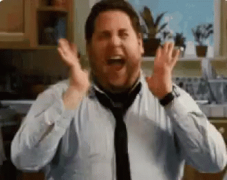 A Man In A Tie Is Laughing With His Hands In The Air In A Kitchen . GIF
