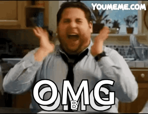 A Man In A Tie Is Making A Funny Face With His Hands In The Air And The Words Omg B On His Chest . GIF