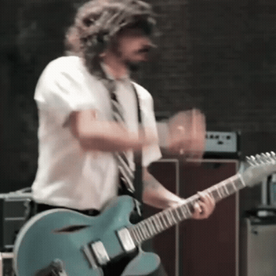 A Man In A Tie Is Playing A Guitar GIF