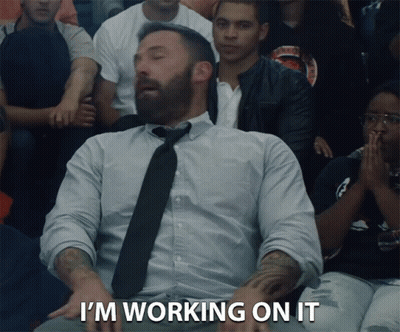 A Man In A Tie Says I 'M Working On It In Front Of A Crowd Of People GIF